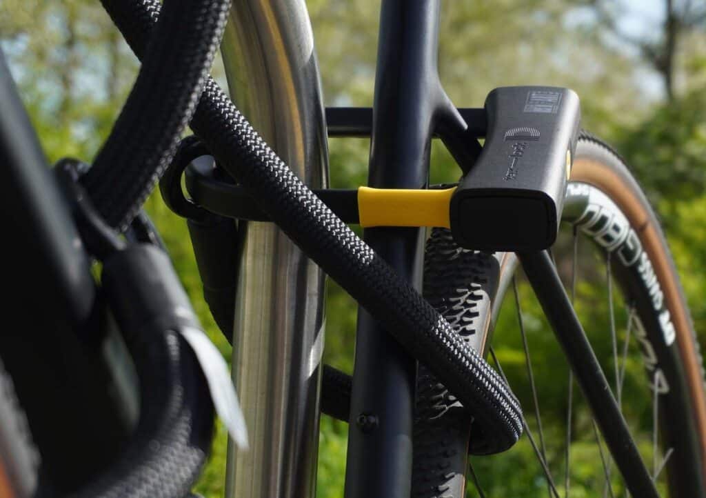 D-lock Bügelschloss sichert Sattelstange und Sattelstrebe mit Textilseil in Farbe onyx black am Fahrradständer